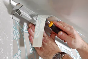 Tapezier-Arbeiten - Decor-Union Service 034a Maler schneidet fachgerecht Tapete für den passgenauen oberen Wandabschluss